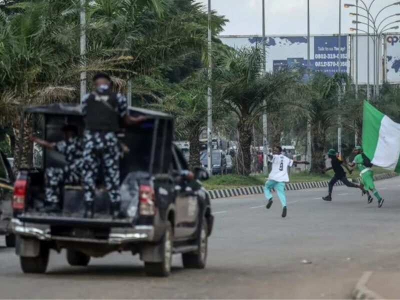 Protesters Carrying A Large Nigerian Flag Run For Safety After Police Fire Tear Gas At Demonstrators In Abuja, On October 1, 2024